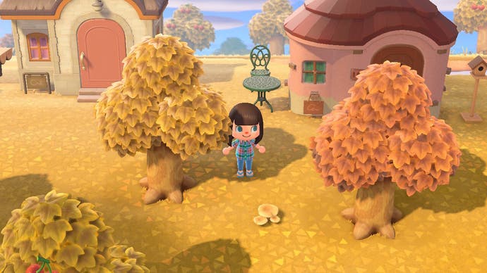 An Animal Crossing: New Horizon screenshot. A small toy-like Animal Crossing character stands in a golden yellow and orange wooded area outside a dinky little house. Autumn is here.