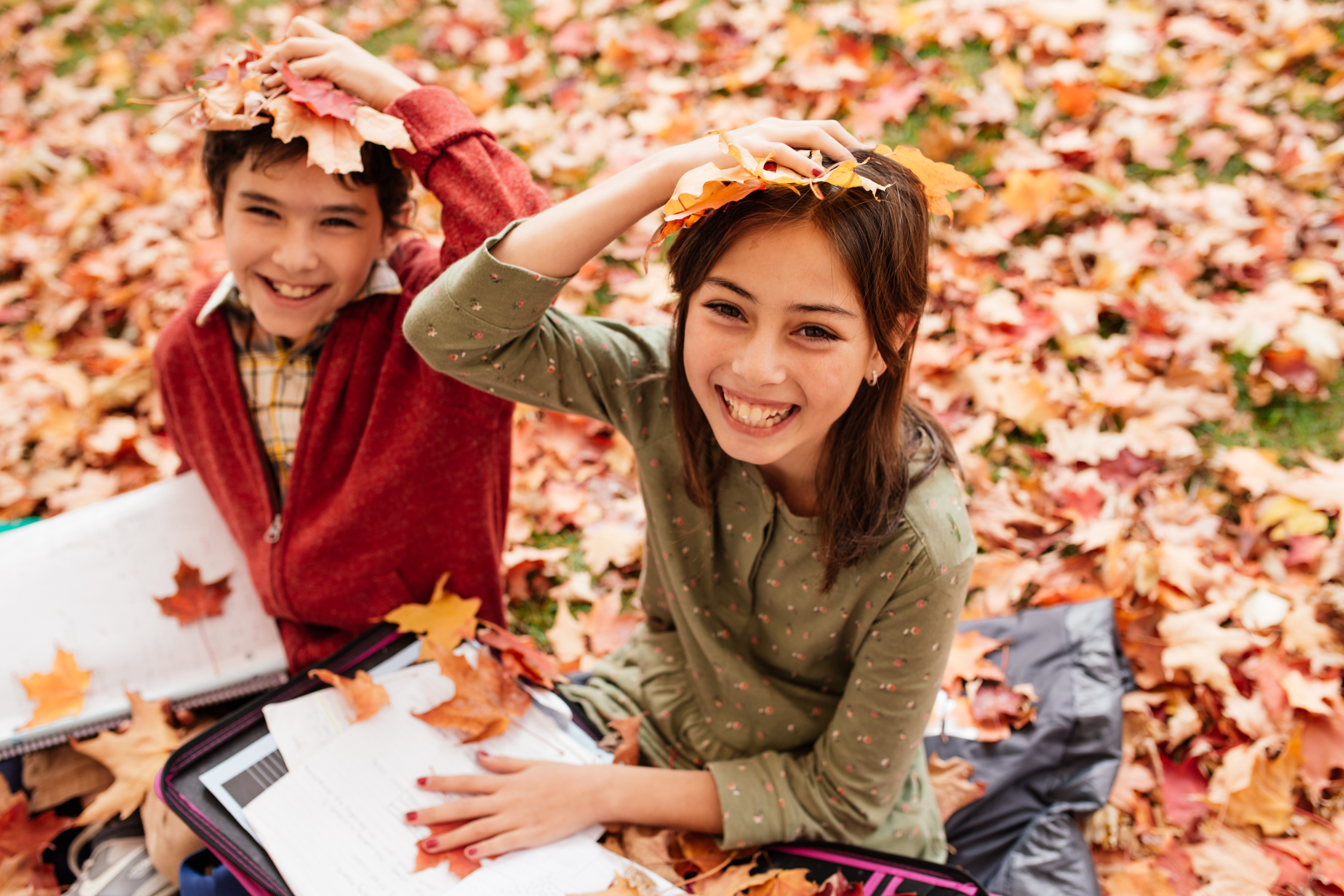 Two middle school students are doing schoolwork outside while surrounded by fall leaves.