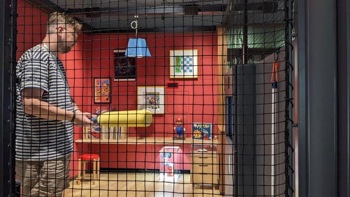 A man holds a soft baseball bat inside the Ultra Machine SP cage in the Nintendo Museum.