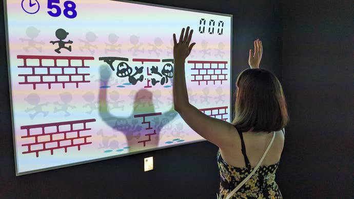 A woman holds up her hands to create platforms in a special Game and Watch game in the Nintendo Museum.