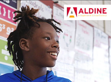 A smiling middle school student at Aldine Independent School District standing in front of board covered with math posters and papers 