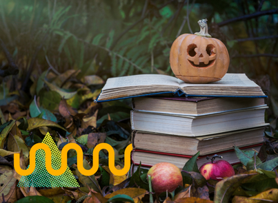 A pile of books with a carved pumpkin on top outside among leaves