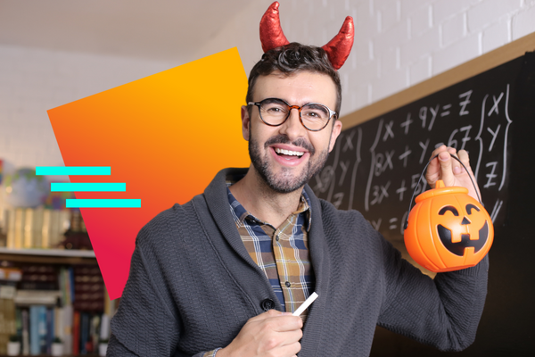 A smiling male teacher in a classroom holding up a carved pumpkin and costume devil horns