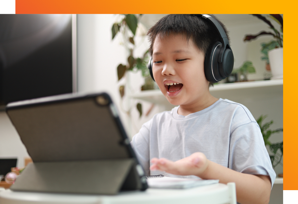 A student happily reading out loud wearing headphones and looking at a tablet