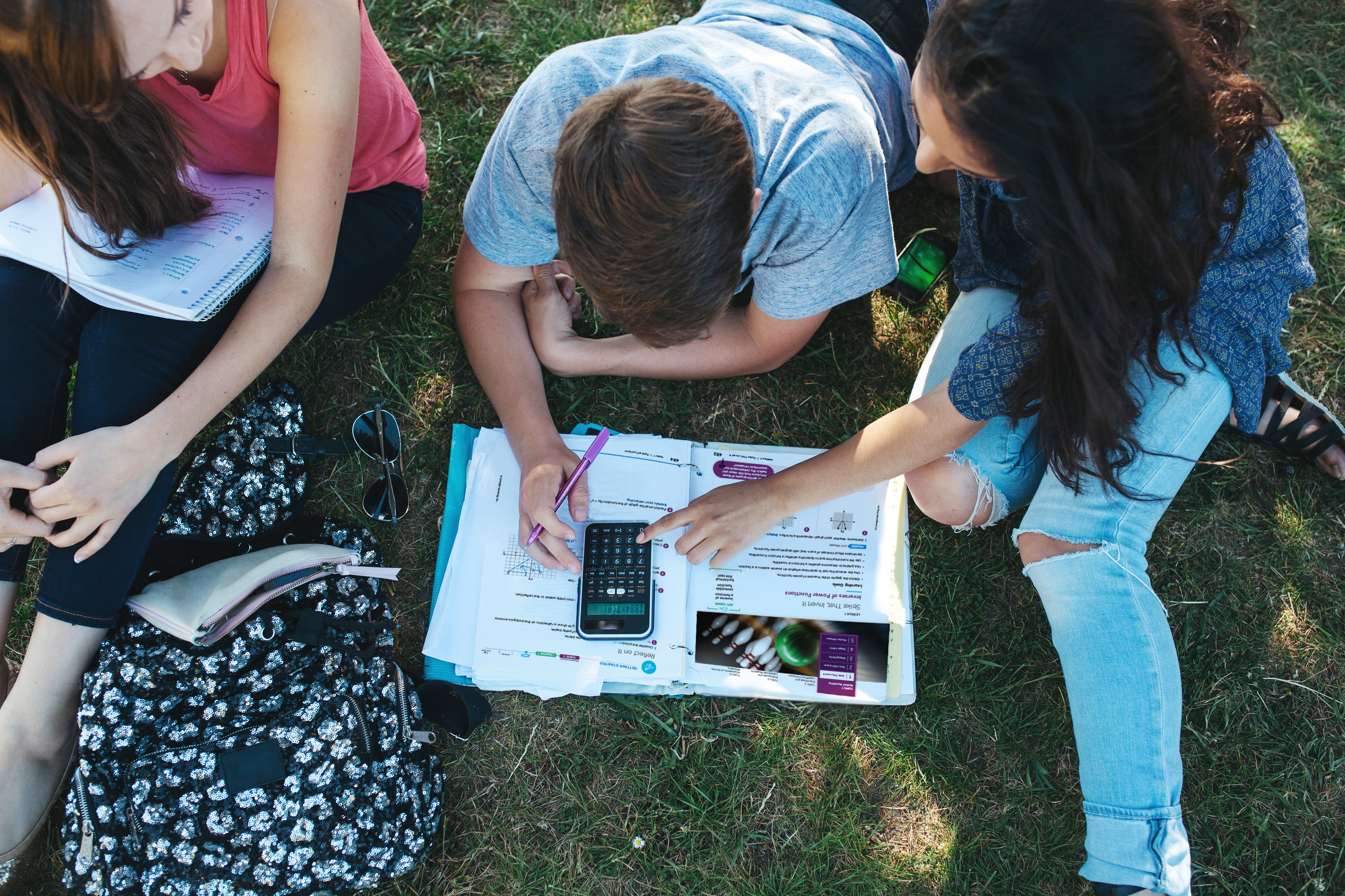 Students are sitting on the grass outside with notebooks and MATHbook.